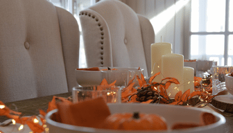 Autumnal table setting with candles, orange leaves and seasonal decorations inside a garden room.